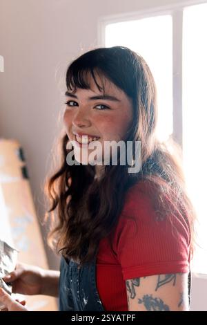 Latin young woman is immersed in painting on canvas in her home studio. Surrounded by natural light, she embodies creativity and passion in a warm, in Stock Photo