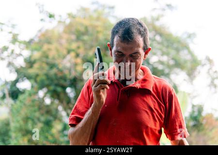 Unrecognizable male farmer using a smartphone during a break, amidst manual labor in the lush Colombian countryside, depicting a blend of traditional Stock Photo