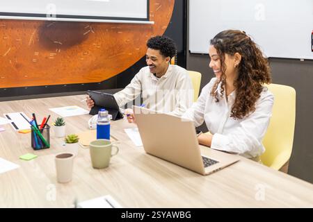 A team engaged in a productive meeting in a modern office. Colleagues are using laptops and tablets at a conference table, fostering collaboration and Stock Photo