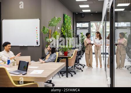 A vibrant office setting featuring a collaborative team discussion and a contemporary open-plan layout. The space is enhanced with natural decor and i Stock Photo