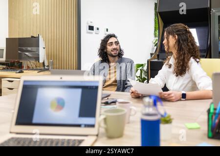 Professionals engaging in a collaborative discussion in a modern open-plan office. Laptops and documents are present, capturing a productive work envi Stock Photo