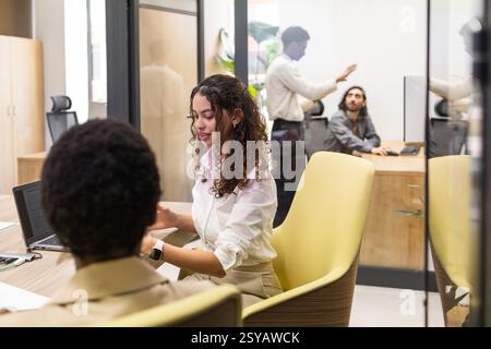 A diverse group of professionals engaged in work within a modern office. Visible are individuals at desks, collaborating and using technology. Bright, Stock Photo