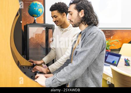 Two colleagues engage in team bonding while enjoying a retro arcade game in a modern office setting, surrounded by work-related materials and collabor Stock Photo