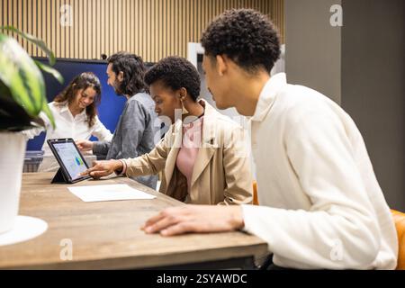 A diverse group of colleagues engage in teamwork in a modern office. They focus on digital tablets and charts, fostering innovation, collaboration, an Stock Photo