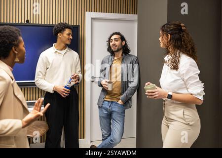 Group of colleagues in a contemporary office setting, engaged in a casual conversation during a coffee break. Modern decor enhances the relaxed atmosp Stock Photo