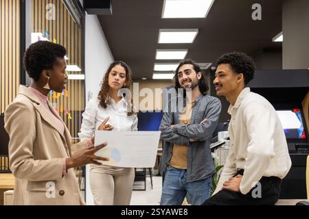 A diverse group of professionals engaged in a team meeting in a modern office. They are discussing a project, with one person holding a document, indi Stock Photo