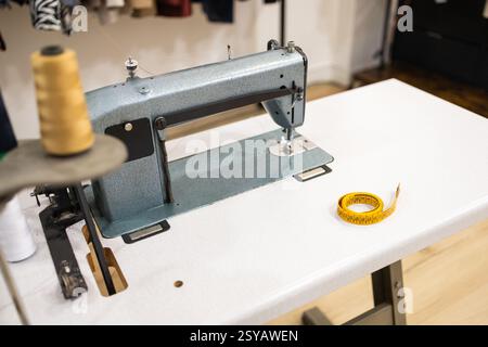 Close up of a vintage sewing machine on a white table with a yellow measuring tape in a suit store. Ideal for themes related to tailoring, fashion des Stock Photo