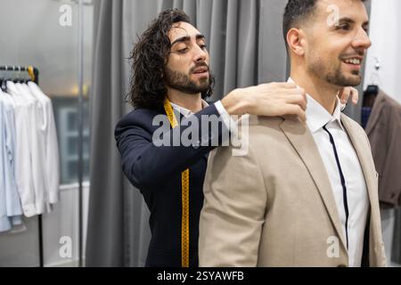 A tailor is attentively adjusting a client suit jacket in a suit store. The focus is on precision and creating the perfect fit for the customer. Stock Photo