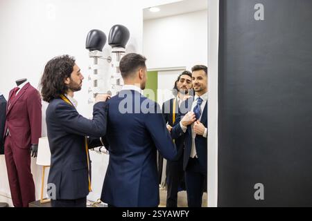 A tailor adjusts a client suit in front of a mirror, ensuring an impeccable fit in a suit store. The tailoring shop showcases various suits, highlight Stock Photo