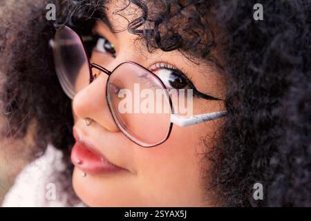 Close-up view of a latin woman wearing round glasses and showcasing curly hair. Her captivating eyes and confident expression convey individuality and Stock Photo