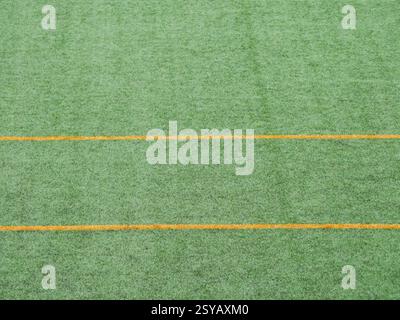 Close up view of green artificial turf featuring parallel yellow lines. Ideal for soccer fields, emphasizes texture and vibrant color. Suitable for de Stock Photo