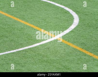 A close up of white and yellow lines marking a soccer field on artificial green turf. The detailed view highlights the texture and precise lines used Stock Photo