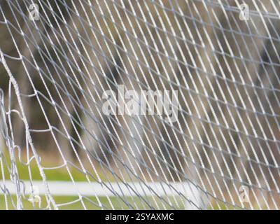 Close up view of a white soccer net in focus, with a blurred natural background. The image captures the texture and pattern of the netting, ideal for Stock Photo