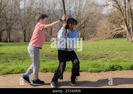 Two friends enjoy a sunny day at the park, playing on a zip line with grassy scenery. The joy of childhood and outdoor play captures the spirit of adv Stock Photo