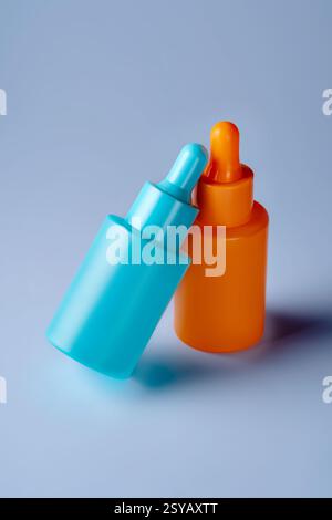 Two vibrant serum bottles in blue and orange hues are showcased against a soothing blue background, emphasizing modern aesthetic and simplicity. Stock Photo