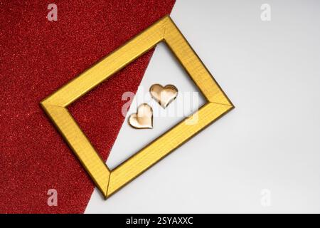 Two golden heart-shaped objects and a rectangular golden frame on a red glittery background, symbolizing love and romance. Stock Photo