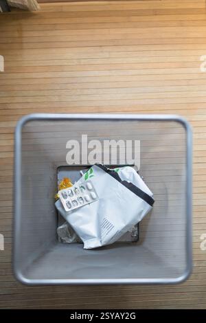 A top down view of a trash bin containing used pill packaging and other waste, set on a wooden floor. This image highlights daily household waste disp Stock Photo