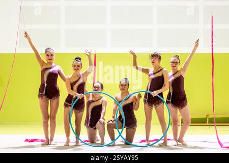 Group of gymnasts whit disability in maroon outfits performing with hoops and ribbons in a brightly lit arena. They showcase elegance, and athleticism Stock Photo
