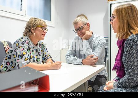 In an office, a women and a couple with intellectual disabilities are engaged in a discussion, sitting around a table. The atmosphere appears thoughtf Stock Photo