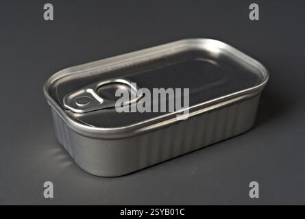 A rectangular metal tin food can with a pull tab lid is placed on a smooth gray background. The can reflective surface catches light, highlighting its Stock Photo