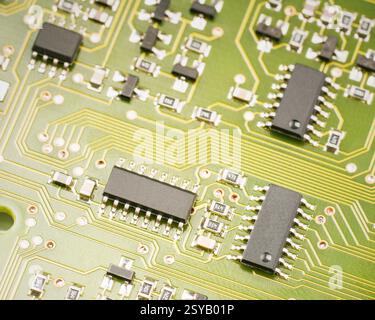 A detailed macro view of a green circuit board showing multiple black microchips and intricate gold pathways, representing technology, hardware, and e Stock Photo