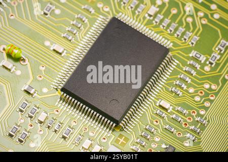A detailed view of a microchip positioned on a green circuit board. The intricate paths and components highlight the complexity of modern electronic d Stock Photo