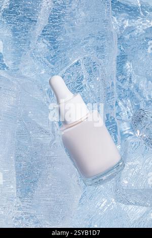 A frosted glass serum bottle with a dropper, cradled by sparkling chunks of ice, emphasizing cooling skin-care treatments. Stock Photo