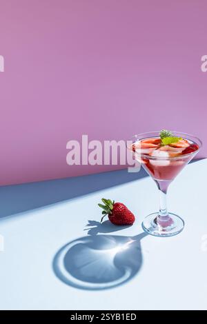 A refreshing strawberry cocktail served in a martini glass, beautifully arranged on a gradient pink and blue background with a lone strawberry and int Stock Photo
