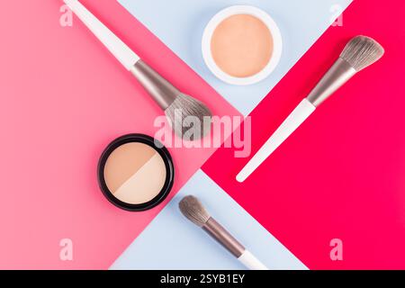 Top view of makeup brushes and face powders arranged on a vibrant red, pink and blue geometric background. Ideal for beauty, fashion, and cosmetic the Stock Photo
