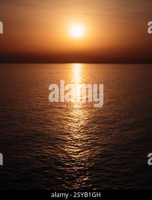 A mesmerizing sunset in Italy casts vibrant orange hues over the tranquil ocean, creating a serene and captivating reflection on the water’s surface. Stock Photo