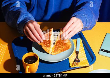 From above, a close-up shot of hands pulling apart a grilled cheese sandwich, revealing melted cheese. Stock Photo