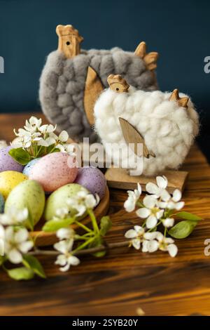 Decorative Easter setup featuring pastel-colored eggs, woolen chicken figures, and delicate white flowers on a wooden table, perfect for seasonal cele Stock Photo