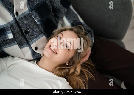 A young woman with a cheerful smile lying next to her cropped unrecognizable partner. She appears relaxed and happy in a casual setting at home lookin Stock Photo