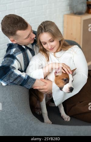 A young couple shares a tender moment with their small dog, conveying warmth and affection in a cozy home environment. Stock Photo