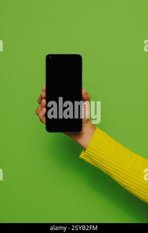 Crop hand of anonymous person holding smartphone with black screen against green background Stock Photo