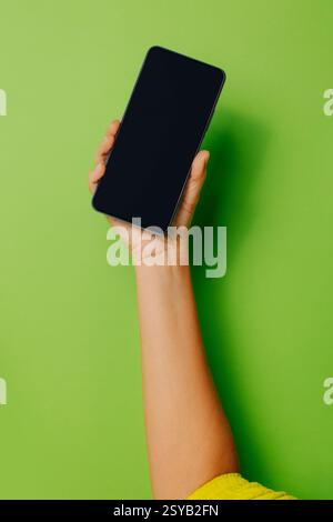 Crop hand of anonymous person holding smartphone with black screen against green background Stock Photo
