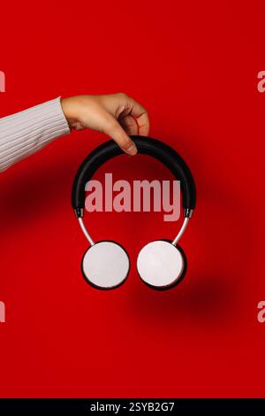 Crop anonymous person holding wireless headphones over red background Stock Photo