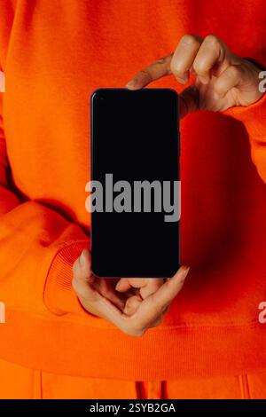 Crop anonymous female in orange casual clothes showing smartphone with empty screen Stock Photo