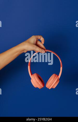 Crop anonymous person holding wireless pink headphones over blue background Stock Photo