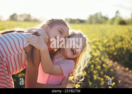 Two girls sisters play happily together in nature on a flowering field in summer Stock Photo