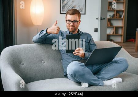 With graphic tablet. Male freelance worker is using laptop at home. Cozy apartment. Stock Photo