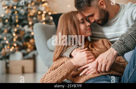 Laying down on the sofa and embracing. Lovely young couple are celebrating New Year at home. Stock Photo