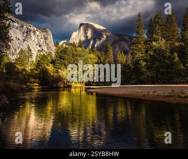 Dramatic sunset over rock formations, including Half Dome, in Yosemite National Park, California, reflecting in Merced Rive; stormy sky in background Stock Photo