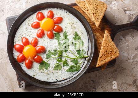 Flower shaped breakfast idea cooked fried eggs, parsley and cherry tomatoes close-up in a plate on the table. Horizontal top view from above Stock Photo
