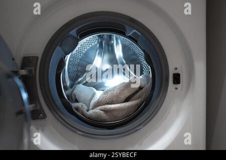 Opened washing machine drum with towel. Closeup. Front view. Washing dirty clothes in the washer. Stock Photo