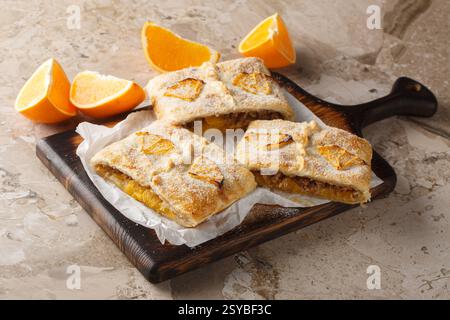 Orange strudel stuffed with walnuts, jam, raisins and fresh fruits close-up on a wooden board on the table. Horizontal Stock Photo