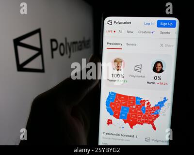 Germany. 27th Nov, 2024. In this photo illustration, a person is holding a cellphone with the webpage of crypto prediction market company Polymarket on screen in front of logo. (Credit Image: © Timon Schneider/SOPA Images via ZUMA Press Wire) EDITORIAL USAGE ONLY! Not for Commercial USAGE! Stock Photo