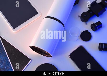 Detail of parts of a disassembled telescope on a white table with electronic devices such as mobile phone and tablet and photos illuminated with blue Stock Photo