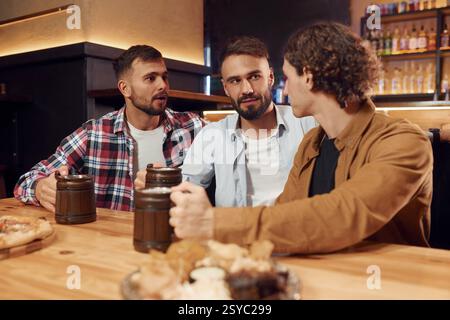 Having a conversation. Three friends are in the bar drinking beer and having a good time. Stock Photo