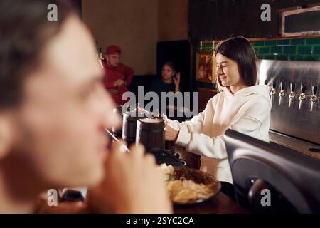 Female bartender holding wooden cups with beer for the customer. Stock Photo